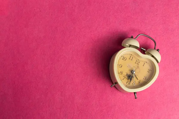 Alarm clock in the shape of a heart on a pink background
