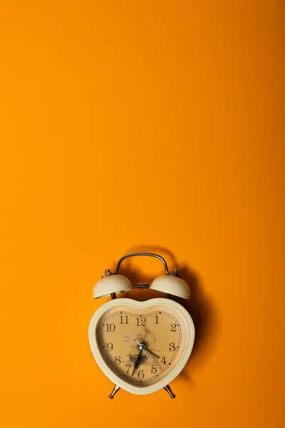Alarm clock in the shape of a heart on a yellow background