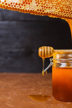 Koyu arkaplanda doğal bal petekleri olan bir kavanoz bal.