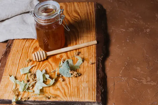 Arkaplanda kuru ıhlamur yaprakları olan bir kavanoz bal.