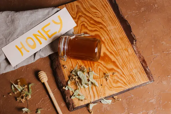 Arkaplanda kuru ıhlamur yaprakları olan bir kavanoz bal.