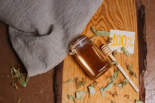 Arkaplanda kuru ıhlamur yaprakları olan bir kavanoz bal.