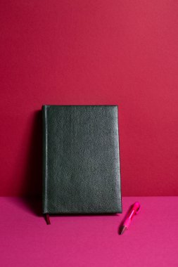 Pembe arka planda kalem olan bir defter..