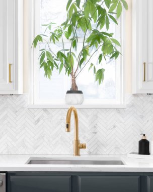 Lüks bir mutfakta, ringa kemikli fayanslarla çekilen lavabo ayrıntıları. Beyaz mermer tezgah ve altın musluk..