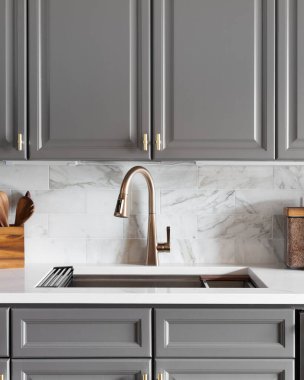 Mutfak lavabosu, gri dolaplar, beyaz mermer tezgah ve süslemeler..