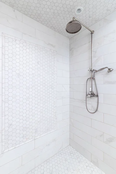 A walkin- shower in a luxury bathroom with hexagon and subway tiles and a chrome faucet.