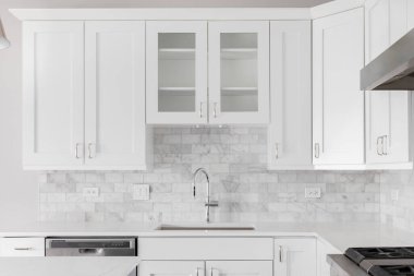 Beyaz dolaplar ve mermer metro döşemeleri ile çekilmiş bir mutfak lavabosu..