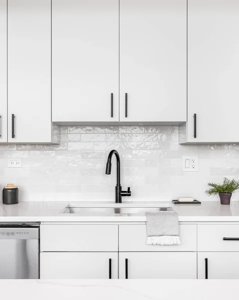 stock image A beautiful white kitchen detail shot with a tiled backsplash, white cabinets, stainless steel appliances, and black hardware and faucet.