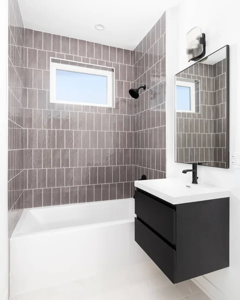 A renovated bathroom with vertical subway tiles, a dark vanity cabinet, and black faucet on a white sink.