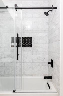 A remodeled glass shower with marble subway tiles, a shelf with black hexagon tiles, and a sliding glass door with black hardware. clipart