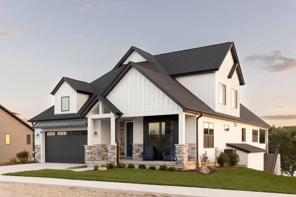 stock image ELMHURST, IL, USA - SEPTEMBER 25, 2022: A black and white luxury home with a two car garage and black door, professional landscaping, and a lake in the background at sunset.