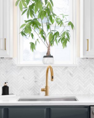 Lüks bir mutfakta, ringa kemikli fayanslarla çekilen lavabo ayrıntıları. Beyaz mermer tezgah ve altın musluk..