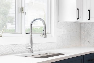 Mutfak lavabosu ayrıntıları mavi ve beyaz dolaplar, ringa kemiği döşemesi ve pencerenin önünde krom musluk..