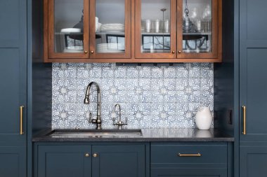 Krom musluk, siyah granit tezgah ve mavi ve ahşap dolaplarla çevrili güzel desenli bir lavabo..