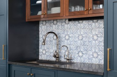 Krom musluk, siyah granit tezgah ve mavi ve ahşap dolaplarla çevrili güzel desenli bir lavabo..