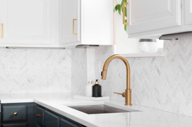 Lüks bir mutfakta, ringa kemikli fayanslarla çekilen lavabo ayrıntıları. Beyaz mermer tezgah ve altın musluk..