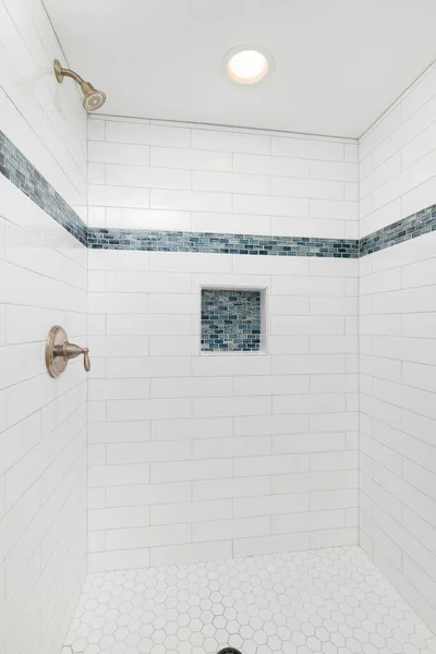 A shower with white and blue subway tiles, bronze faucet, and a white hexagon tile floor.