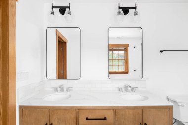 A beautiful bathroom with a wooden cabinet, marble countertop, subway backsplash, and black lights above the mirrors.