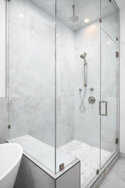 A luxury shower with marble walls, chrome faucets, and a marble hexagon tiled floor.