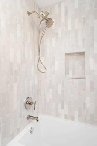 An empty shower with vertical brown subway tiles and small, a built-in shelf, with a gold shower head and faucet.