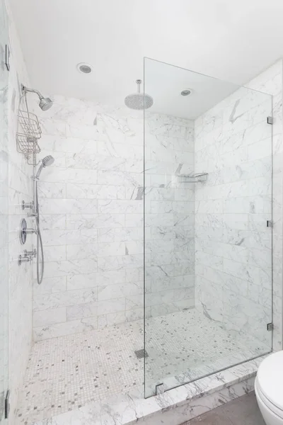 A walk-in shower with marble subway tile walls, square tiled floor, and a chrome shower head.