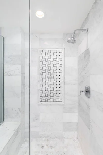 A shower with marble subway and hexagon tiles, an interlocking tile pattern on the wall, bench seat, and chrome showerhead.
