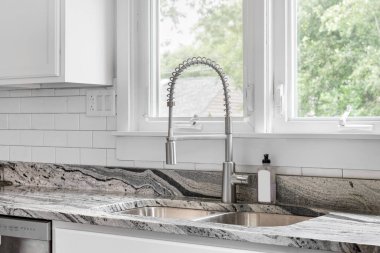 A kitchen sink detail in an all white kitchen with a subway tile backsplash and granite countertops.