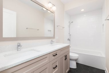 A bathroom with a brown cabinet, black hexagon tile floor, and a subway tile shower.