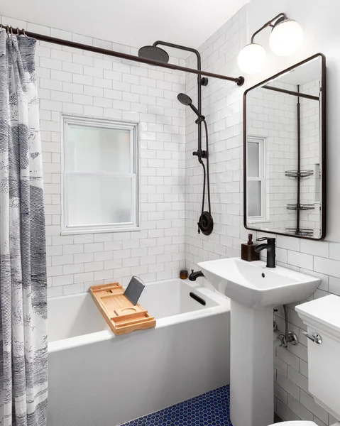 A bathroom with a white subway tile shower and black faucet, blue circular tile floor, and a white pedestal sink.
