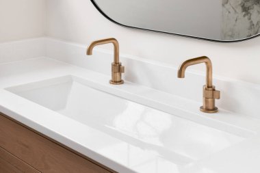 Beyaz meşe dolabı, mermer tezgahı, altın muslukları ve siyah yuvarlak aynası olan güzel bir banyo..