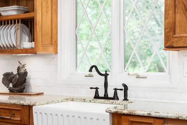 A kitchen faucet detail with a black faucet, white apron sink, wood cabinets, and a white tiled backsplash.