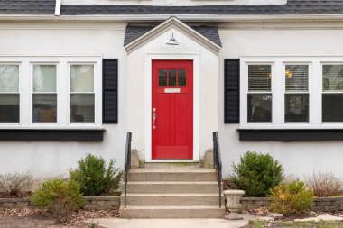 Kapıya kadar uzanan beton merdivenleri ve demir parmaklıkları olan beyaz bir evin kırmızı ön kapısı..