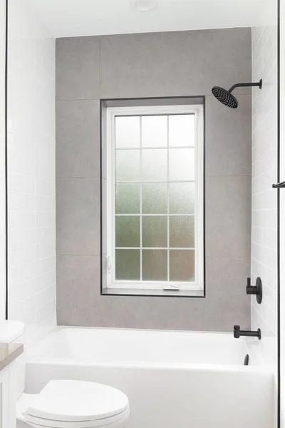 A luxury shower with white subway and brown tile walls, black faucet, and a white framed window with frosted glass.