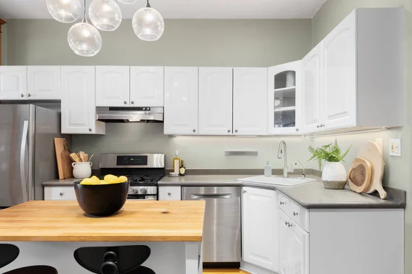 A kitchen detail with white cabinets, wood butcher block island, green walls, and a light fixture hanging above. No brands or labels.
