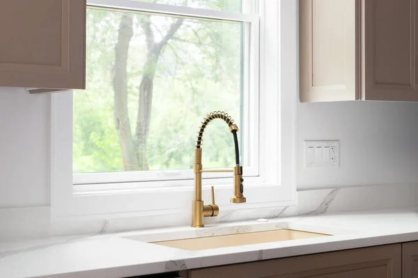 stock image A gold kitchen faucet detail with a gold sink, brown cabinets, and a white marble countertop.