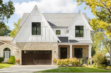 Oak Park, IL, ABD - 17 Ekim 2020: Gri kiremitli çatı ve siyah pencere çerçeveli yeni, beyaz, modern bir çiftlik evi. Evin altında hafif bir kaya kaplaması ve verandası var..