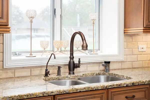 A bronze kitchen faucet detail with wood cabinets, stone subway tile backsplash, and a granite countertop.