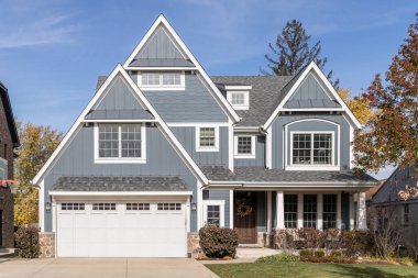 Barrington, IL, ABD - 7 Kasım 2023: Kapalı verandası, gri çatısı ve iki araba garajı olan mavi ve beyaz bir çiftlik evi.