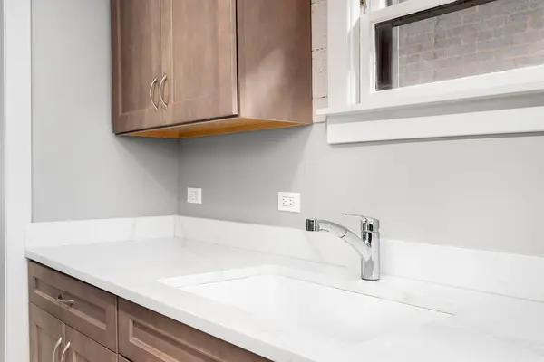 A kitchen faucet detail with a marble countertop, wood cabinets, and a chrome faucet.