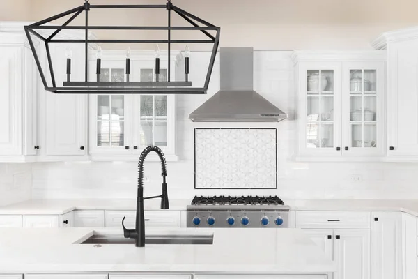 A kitchen detail with a black faucet and light fixture on the island, white cabinets, and a mosaic tile backsplash. No brands or logos.