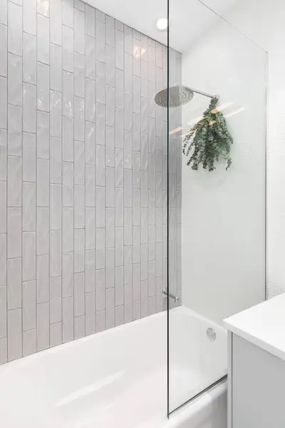 A shower detail with grey vertical subway tiles, white circular tiles, and eucalyptus hanging from the chrome showerhead.