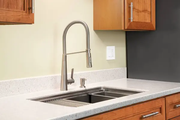 A kitchen faucet detail with a quartz countertop, wood cabinets, and a stainless single handle faucet.