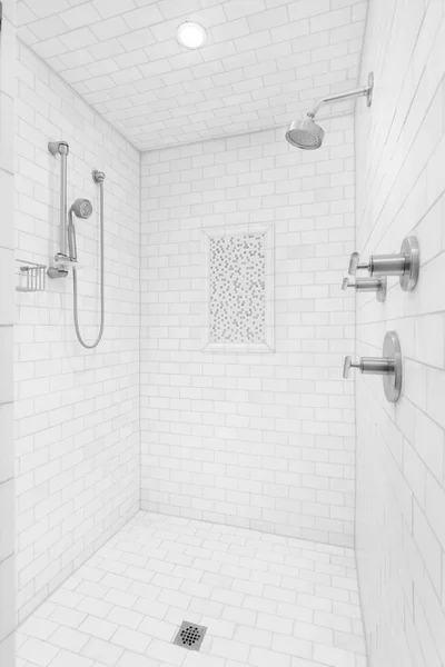 A large walk-in shower with subway tiles on the walls and floor, chrome shower heads and faucet, and a small square tile accent.