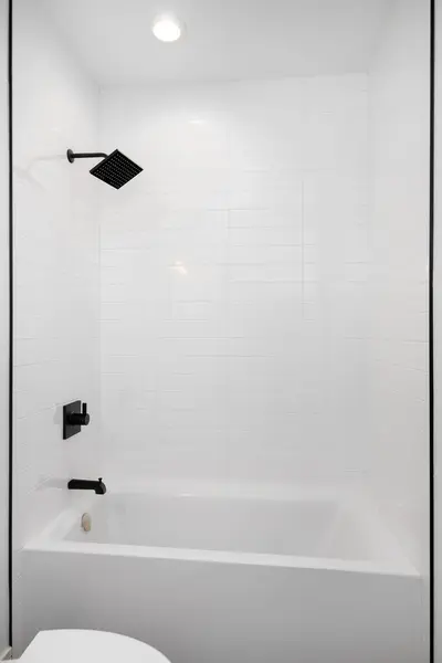 A shower and bathtub with white subway tiles and black showerhead and faucet.