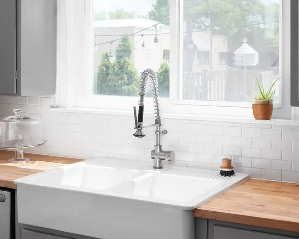A kitchen sink detail with a butcher block wood countertop, white subway tile backsplash, grey cabinets, and a farmhouse sink.