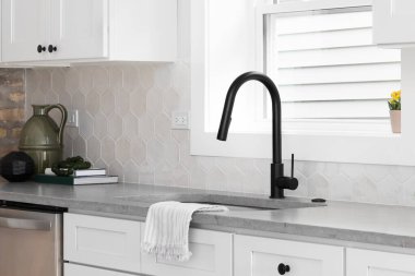 A beautiful kitchen sink detail with white cabinets, marble countertops, and a hexagon tiled backsplash.