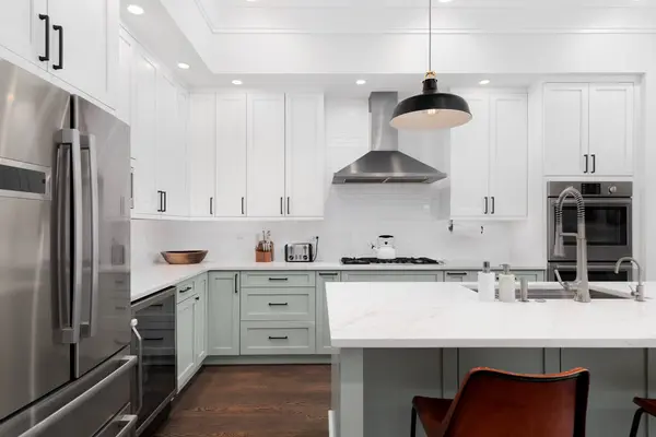 A kitchen detail with white and sage green cabinets, a large island, subway tile backsplash, and stainless steel appliances. No brands or logos.