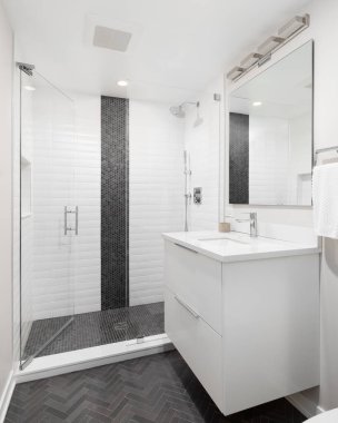 Beyaz dolabı olan bir banyo, kömür, ringa kemiği döşemesi ve beyaz metro ve siyah dairesel fayanslarla dolu bir duş..