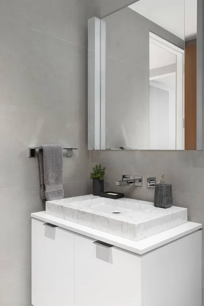 A bathroom sink detail with a white marble vessel sink, white cabinet, and grey stone tile walls.