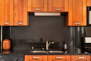 Ahşap dolapları ve siyah galaksi granit tezgahı olan bir mutfak musluğu..
